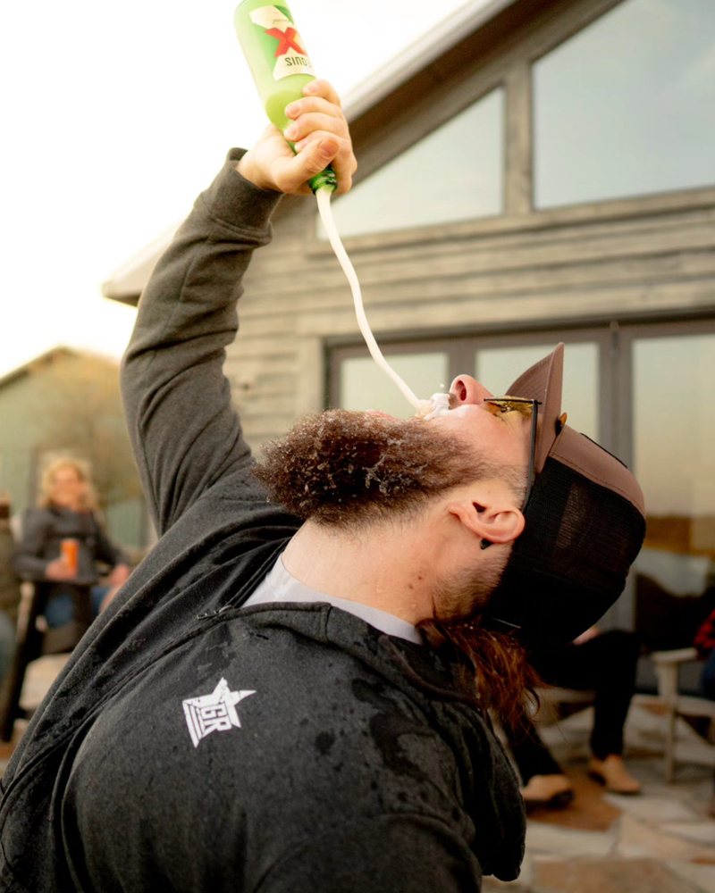 Gast trinkt vor einer Berghütte, Freunde schauen zu